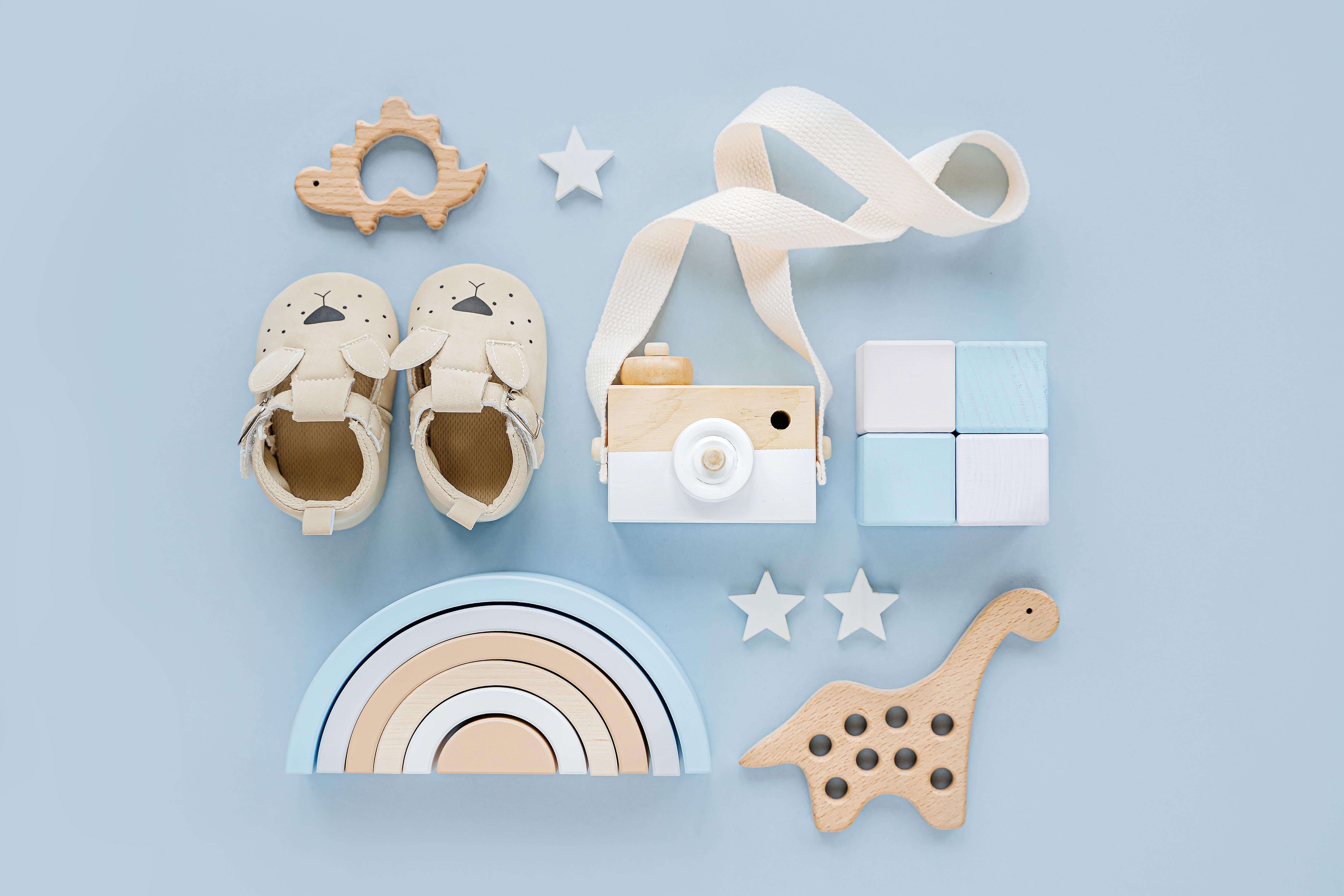 Baby essentials including shoes, wooden toys, and a toy camera on a light blue background